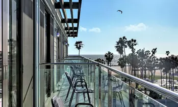 Ocean view balcony with chairs and palm trees.