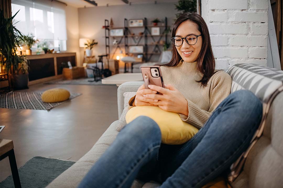 Woman smiling at phone on couch.